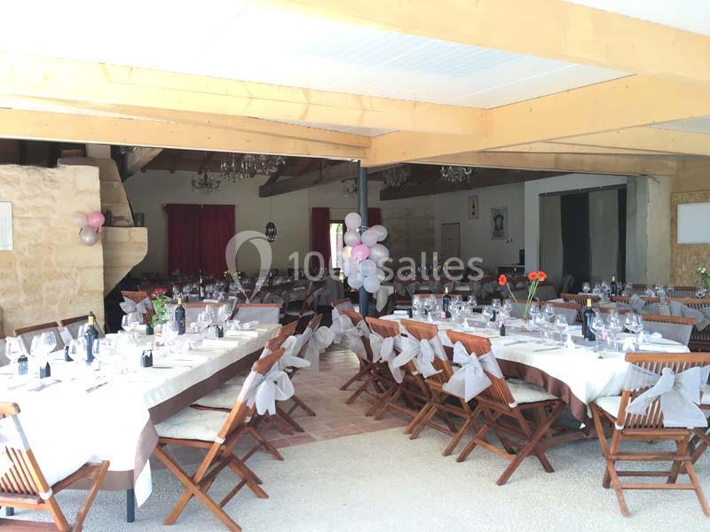 Salle de réception décorée avec des tables dressées, chaises en bois et ballons, prête pour un événement festif.