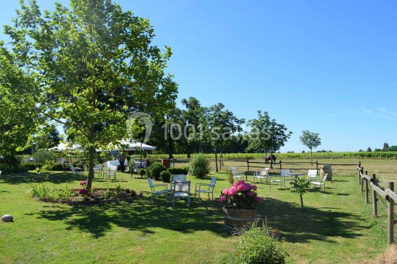 Jardin aménagé avec tables et chaises, entouré de verdure et bordé de champs sous un ciel bleu clair.