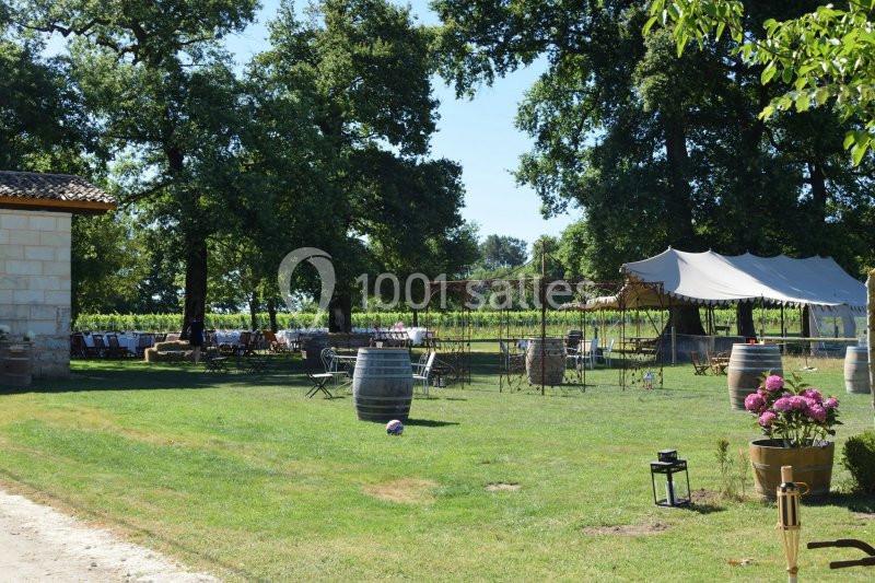 Espace extérieur avec tables, chaises, tonnelle et décor champêtre, entouré de vignes et d'arbres.