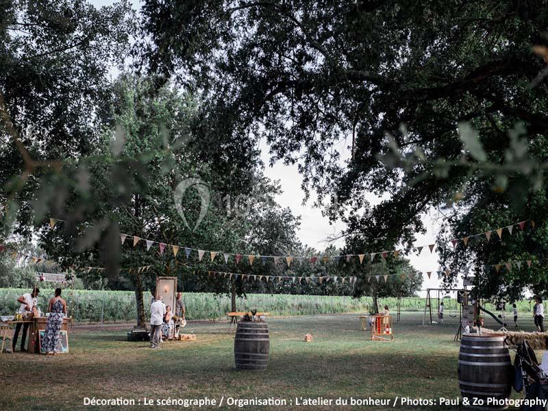 Un espace extérieur décoré avec des guirlandes colorées, des tonneaux et des tables, entouré d'arbres et de verdure.
