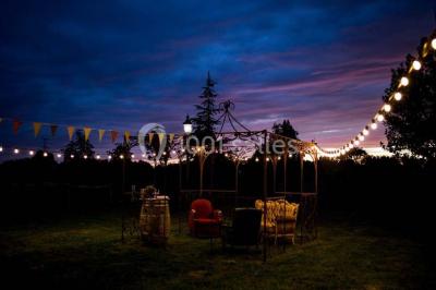 Espace extérieur décoré avec guirlandes lumineuses, fauteuils et tonnelle, au crépuscule dans un jardin.