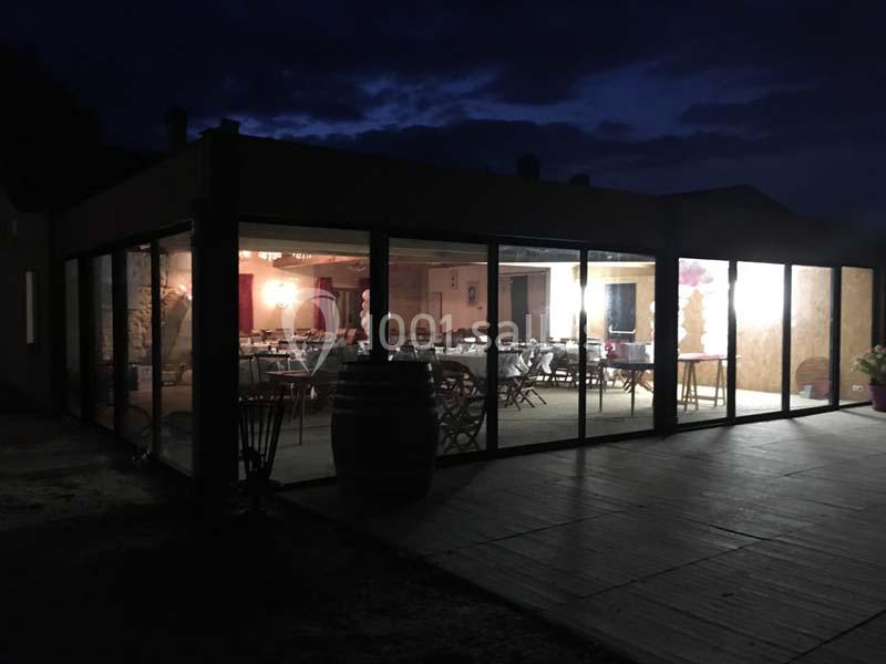 Salle éclairée vue de l'extérieur à travers de grandes baies vitrées, de nuit.