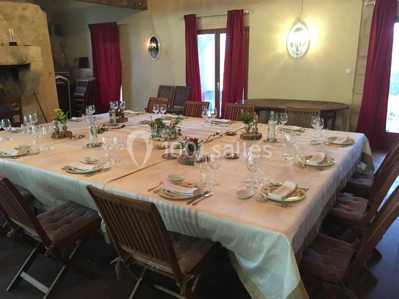 Grande table rectangulaire dressée avec nappes, vaisselle et décorations florales, entourée de chaises en bois.