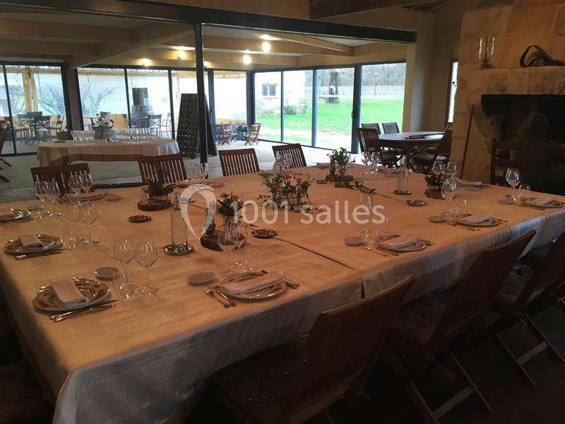 Grande table rectangulaire dressée pour un repas, entourée de chaises en bois, dans une salle lumineuse avec vue sur un…