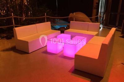 Salle de réception avec tables hautes noires, verres lumineux et éclairage tamisé dans une ambiance festive.