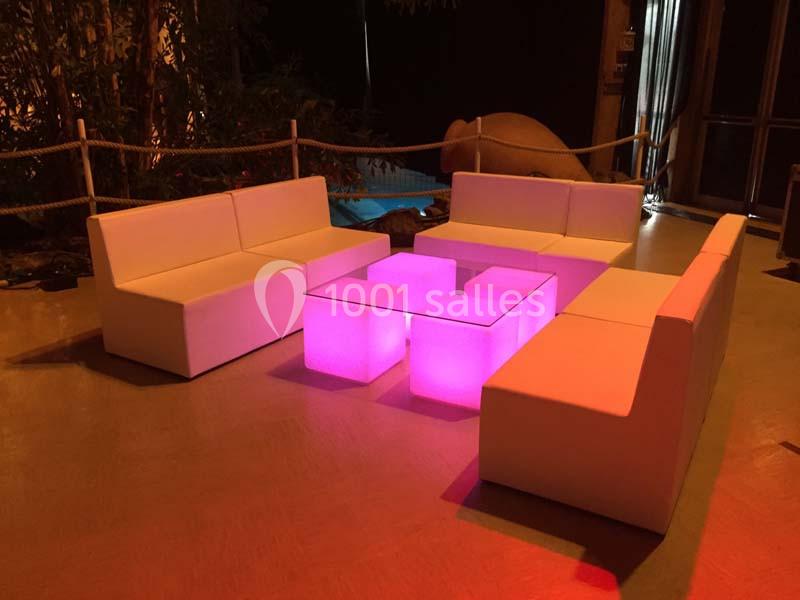 Canapés blancs disposés autour d'une table basse lumineuse rose dans un espace intérieur faiblement éclairé.