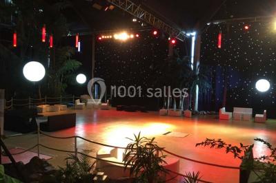 Salle de réception avec tables hautes noires, verres lumineux et éclairage tamisé dans une ambiance festive.