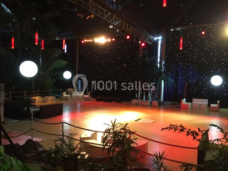 Salle de réception avec éclairage tamisé, décor végétal, mobilier blanc et scène en fond avec rideau étoilé.