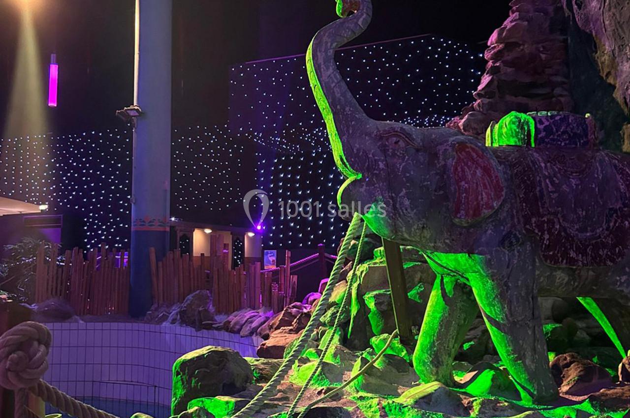 Statue d'éléphant en pierre éclairée par des lumières vertes, entourée de cordes et de décorations dans un espace intérieur…