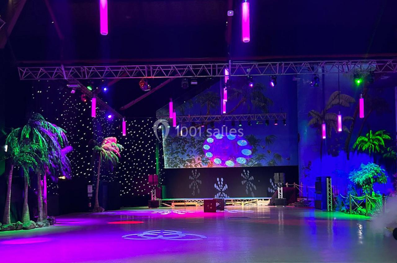 Salle de spectacle décorée avec des palmiers artificiels, éclairages colorés et projecteurs lumineux.