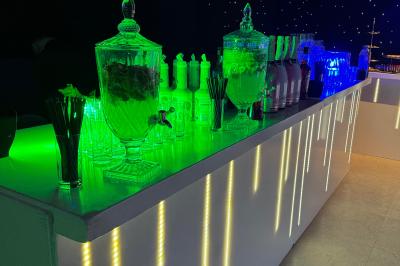 Salle de réception avec tables hautes noires, verres lumineux et éclairage tamisé dans une ambiance festive.