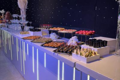 Salle de réception avec tables hautes noires, verres lumineux et éclairage tamisé dans une ambiance festive.