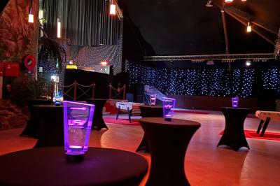 Salle de réception avec tables hautes noires, verres lumineux et éclairage tamisé dans une ambiance festive.