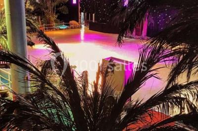 Piscine intérieure décorée de plantes tropicales, éclairée par des lumières colorées et entourée d'un pont en bois.