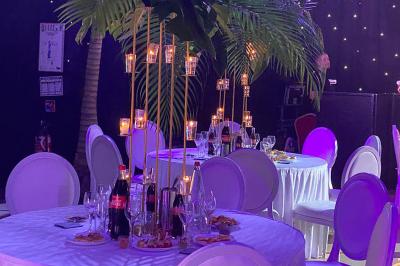 Piscine intérieure décorée de plantes tropicales, éclairée par des lumières colorées et entourée d'un pont en bois.