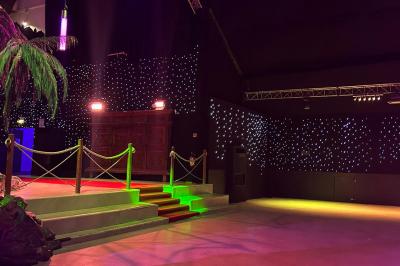 Piscine intérieure décorée de plantes tropicales, éclairée par des lumières colorées et entourée d'un pont en bois.