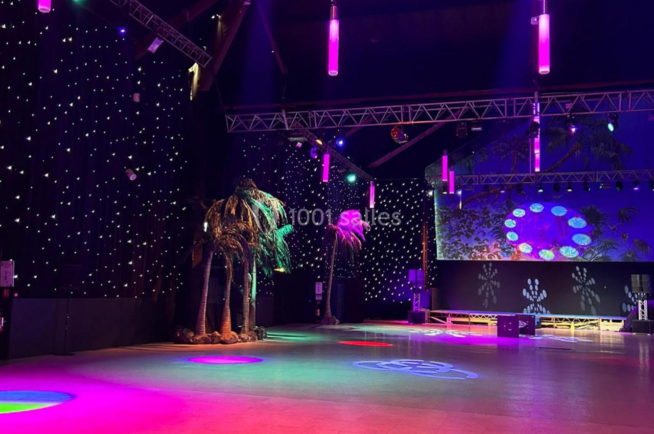 Salle de spectacle avec éclairage coloré, palmiers décoratifs et murs ornés de lumières étoilées.