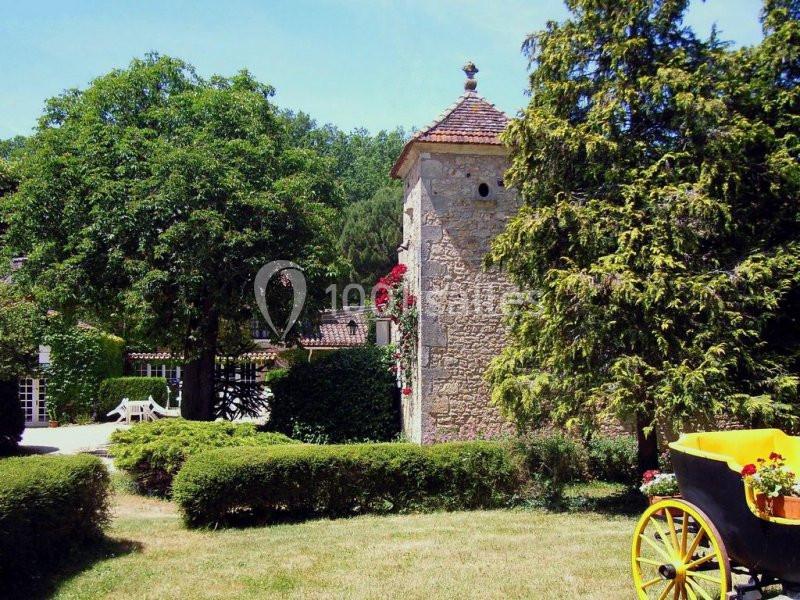 Tour en pierre entourée de verdure avec une calèche jaune au premier plan dans un jardin ensoleillé.