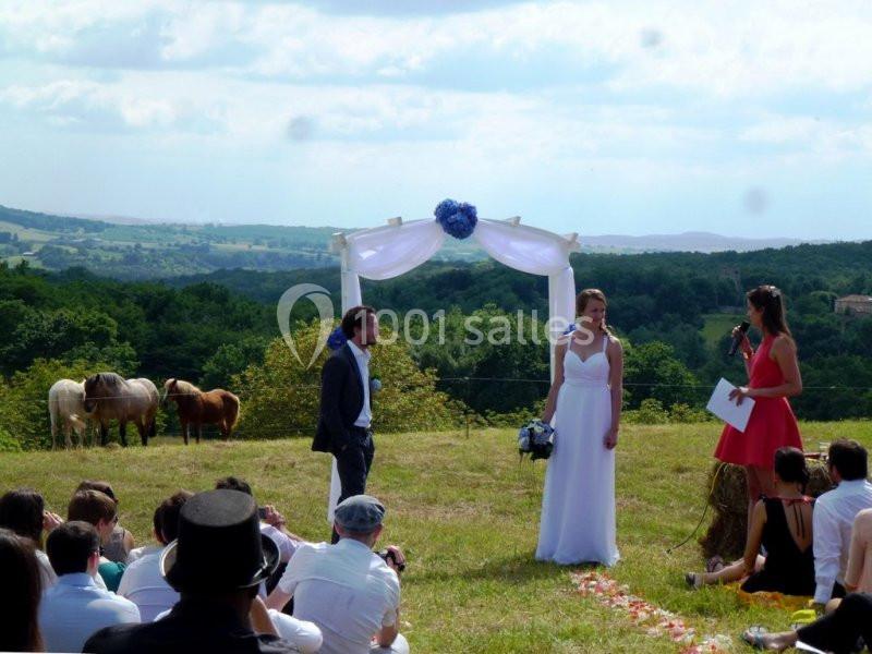 Un couple se tient devant une arche décorée lors d'une cérémonie en plein air, avec des chevaux en arrière-plan.