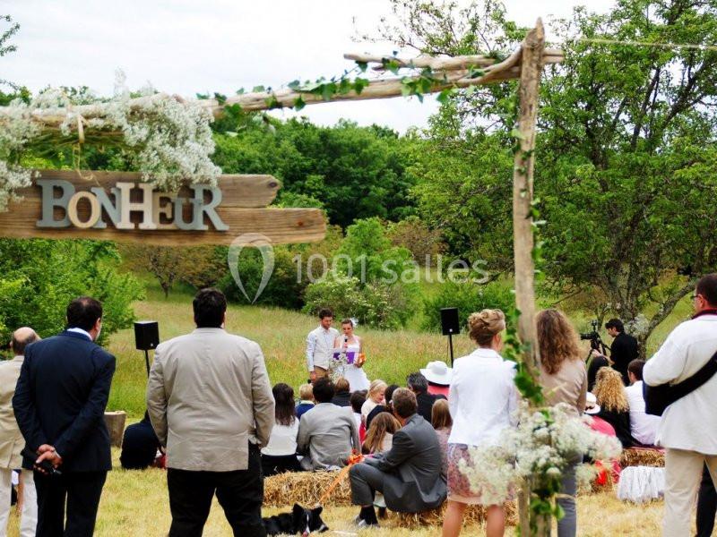 Cérémonie en plein air avec des invités assis sur des bottes de paille, décor champêtre et panneau en bois ’Bonheur’.