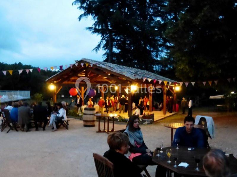 Personnes rassemblées dans une ambiance festive en soirée, sous un pavillon en bois décoré de guirlandes colorées.