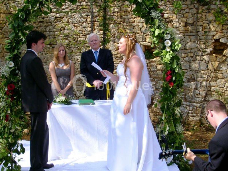 Une cérémonie de mariage en extérieur avec une mariée lisant un texte devant un marié, un officiant et des invités.
