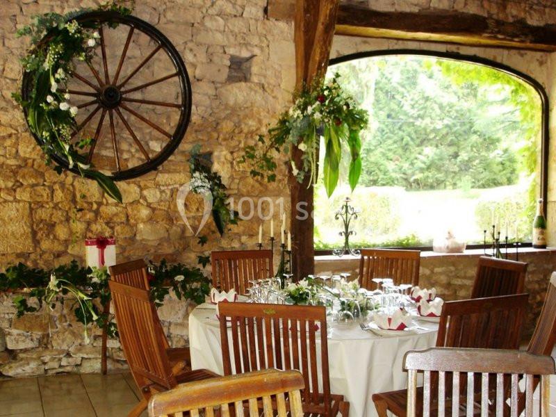 Salle rustique décorée pour un repas, avec des murs en pierre, des chaises en bois et des arrangements floraux.