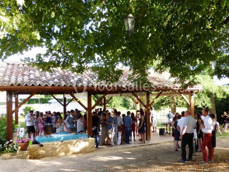 Groupe de personnes rassemblées sous une pergola en bois dans un cadre extérieur verdoyant et ensoleillé.