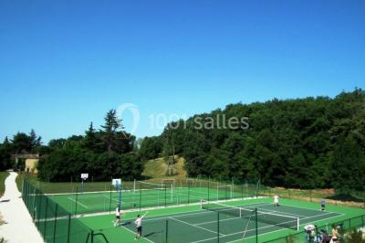 Terrains de tennis extérieurs entourés de verdure, avec des joueurs en action sous un ciel dégagé.