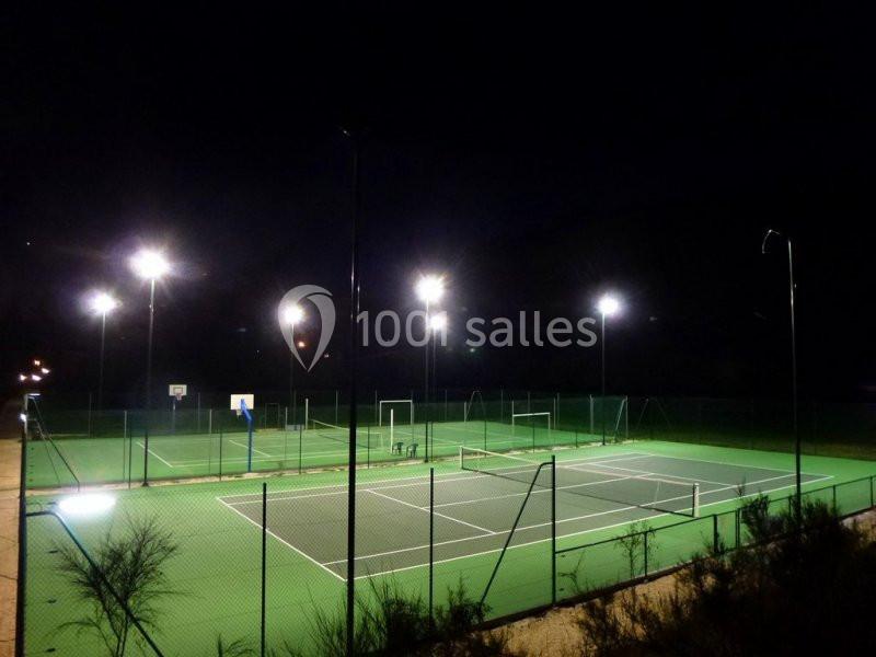 Terrains de sport extérieurs éclairés la nuit, comprenant un terrain de tennis et un terrain de basket.