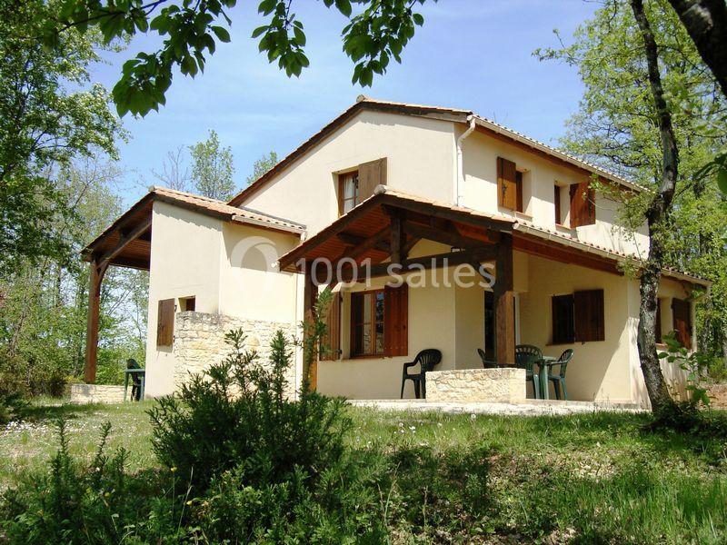 Maison en pierre et crépi beige avec volets en bois, entourée de végétation et équipée d'une terrasse couverte.