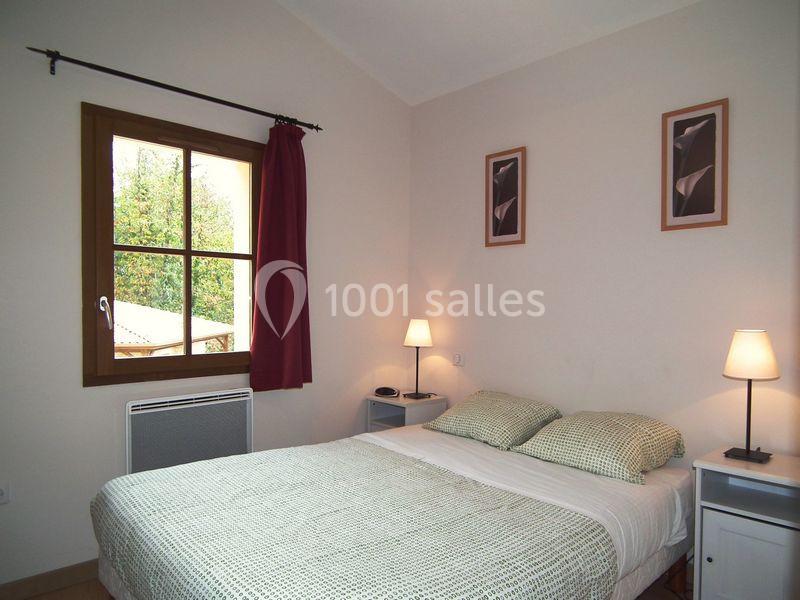 Chambre lumineuse avec un lit double, deux lampes de chevet, une fenêtre avec rideau rouge et des tableaux au mur.