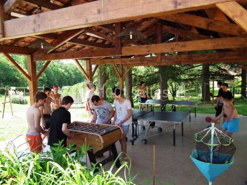 Des jeunes jouent au baby-foot et au tennis de table sous un abri en bois, entouré de verdure.