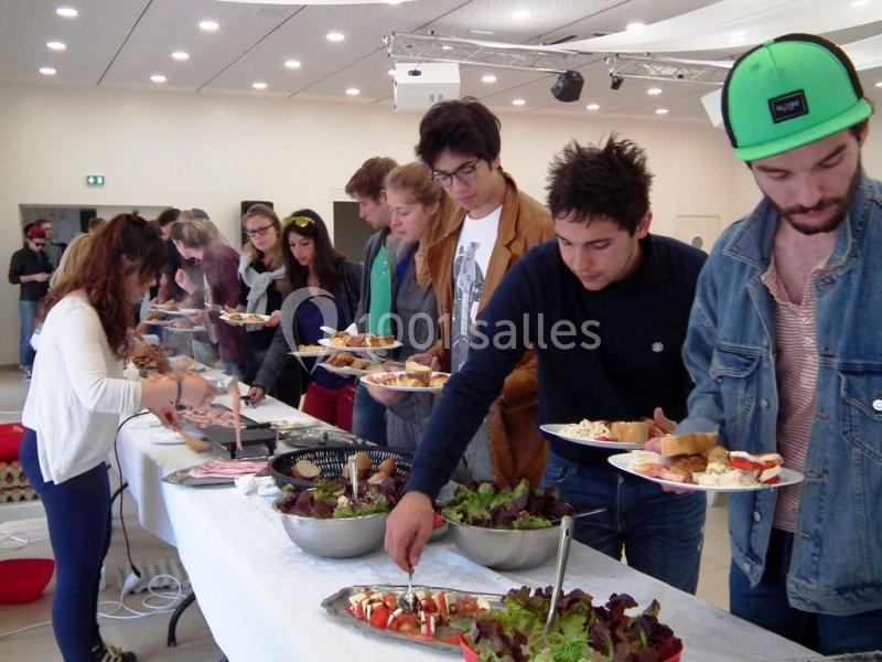 Des personnes se servent à un buffet avec des plats variés, dans une salle lumineuse.