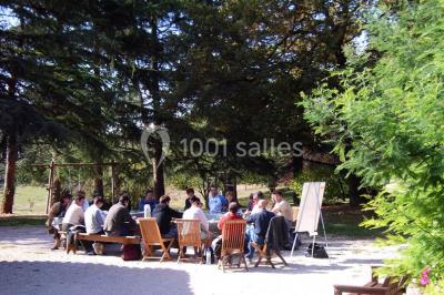 Un groupe de personnes assises en cercle en plein air, discutant près d'un tableau blanc, entouré d'arbres.