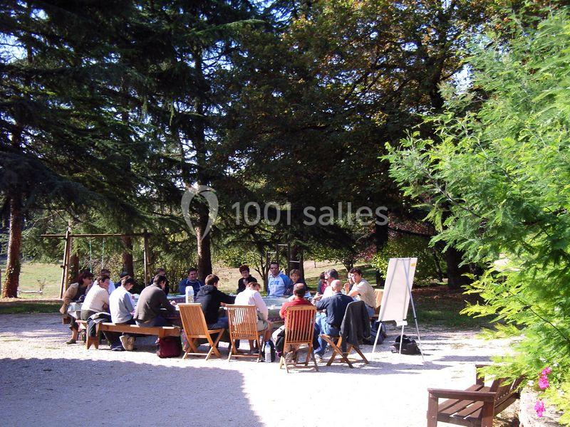 Un groupe de personnes assises en cercle en plein air, discutant près d'un tableau blanc, entouré d'arbres.