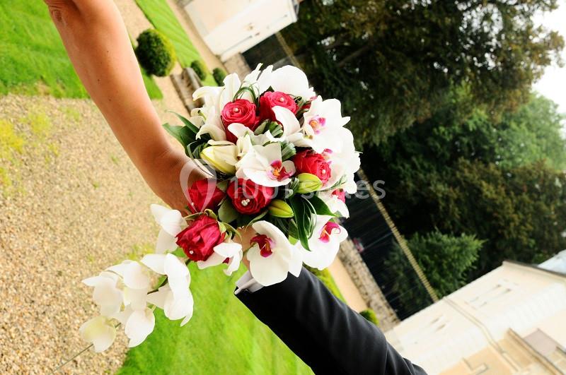 Un bouquet de roses rouges et d'orchidées blanches tenu par deux personnes en extérieur.