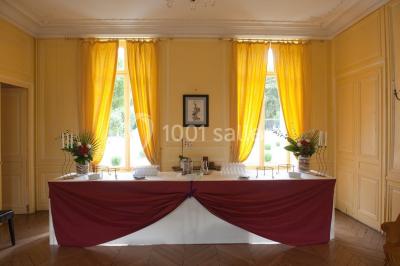 Façade d'un château entouré de jardins bien entretenus, avec un ciel nuageux en arrière-plan.