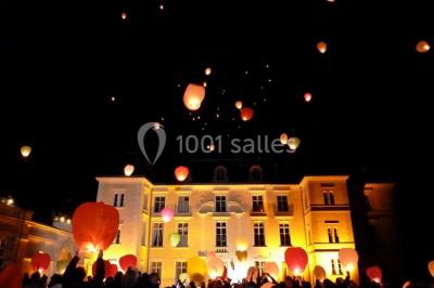 Façade d'un château entouré de jardins bien entretenus, avec un ciel nuageux en arrière-plan.