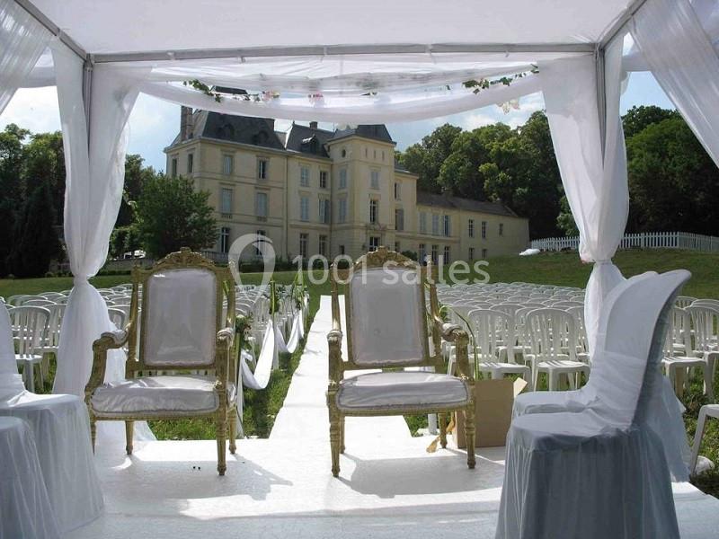 Deux chaises dorées sous une tente décorée, face à une allée bordée de chaises blanches, devant un château.