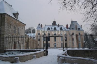 Façade d'un château entouré de jardins bien entretenus, avec un ciel nuageux en arrière-plan.