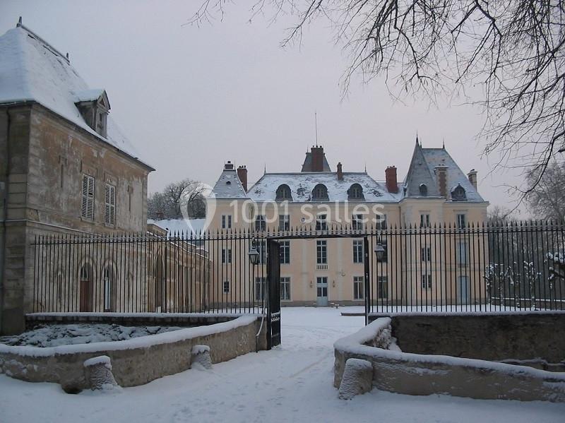 Façade d'un château entouré de grilles en fer forgé, avec un sol et des toits recouverts de neige.