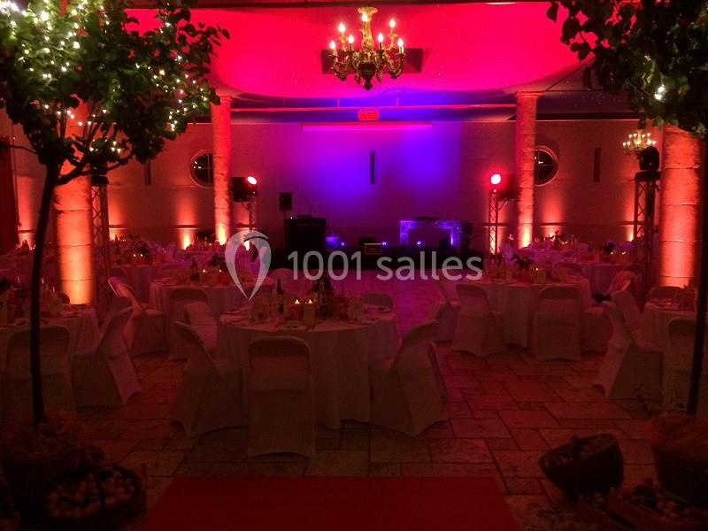 Salle de réception décorée avec des tables rondes, des chaises blanches et un éclairage tamisé aux tons rouges et violets.