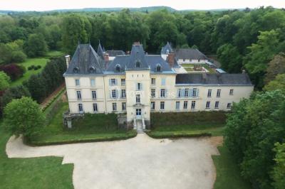 Façade d'un château entouré de jardins bien entretenus, avec un ciel nuageux en arrière-plan.