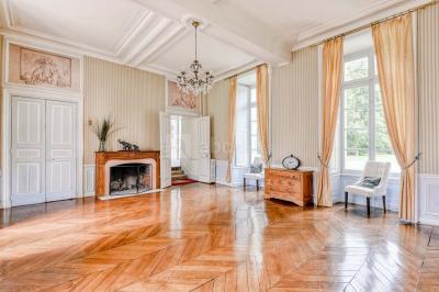 Façade d'un château entouré de jardins bien entretenus, avec un ciel nuageux en arrière-plan.