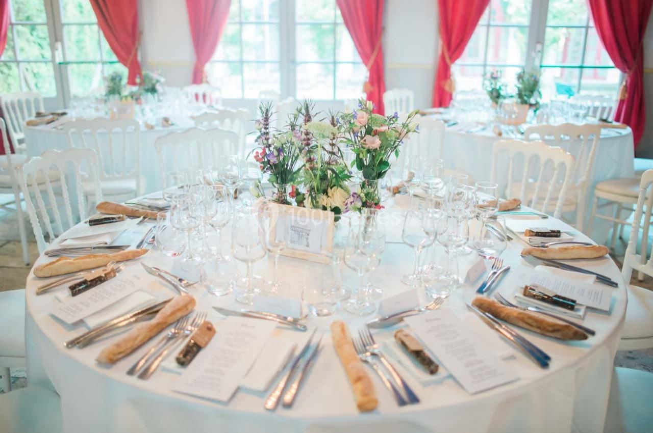 Table ronde élégamment dressée avec nappes blanches, couverts, menus, bouquets de fleurs et baquettes, dans une salle…
