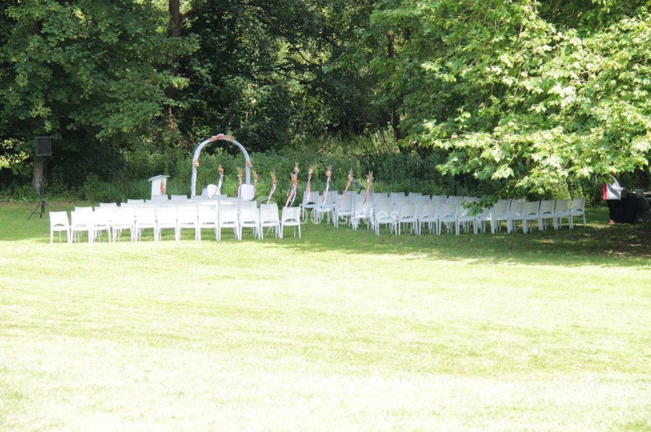 Chaises blanches disposées en extérieur devant une arche décorée, entourées de verdure dans un cadre naturel.