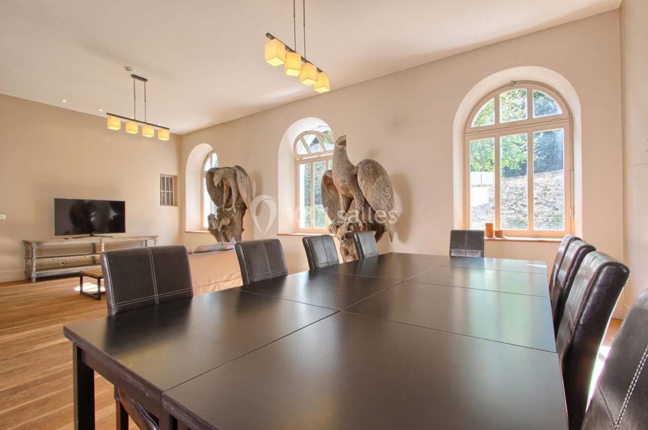 Salle à manger lumineuse avec une grande table noire, des chaises en cuir et des sculptures d'oiseaux près des fenêtres.
