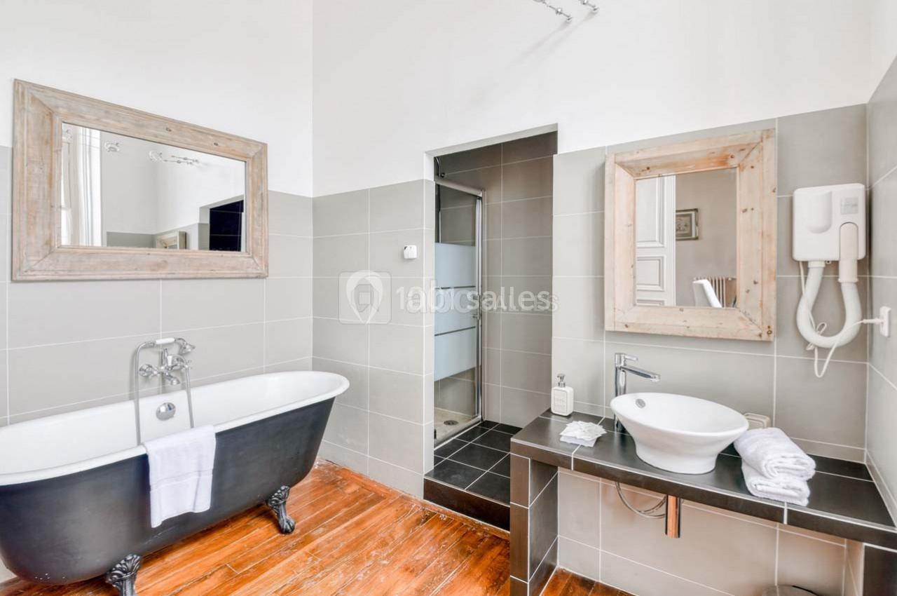 Salle de bain lumineuse avec baignoire sur pieds, douche à l'italienne, lavabo moderne et miroirs encadrés en bois.