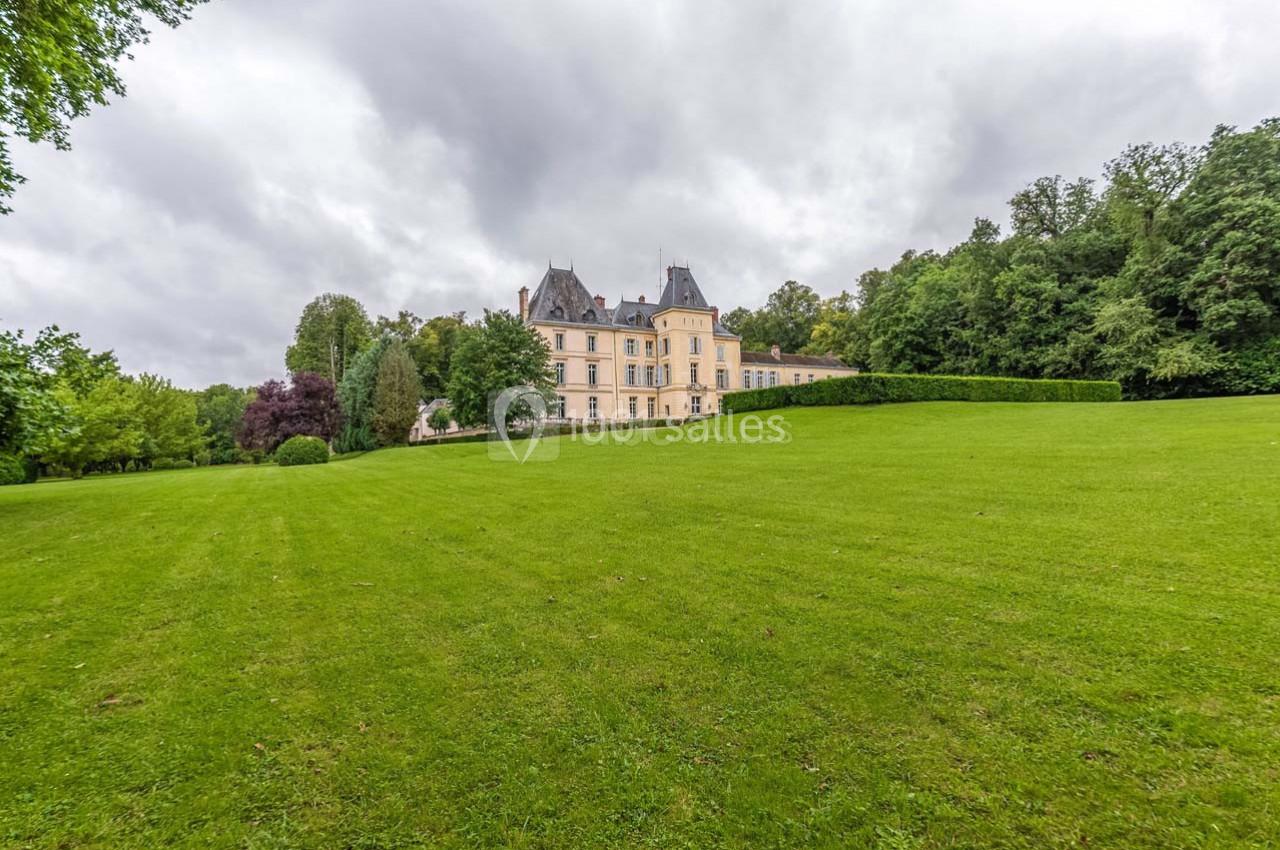 Château entouré d'un vaste parc verdoyant sous un ciel nuageux.